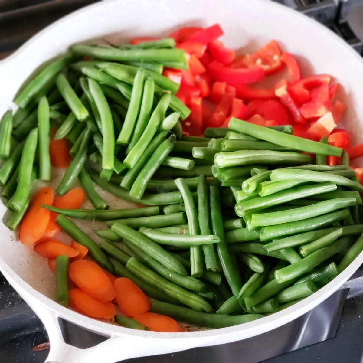 Green beans, carrots and red pepper in a light colored skillet