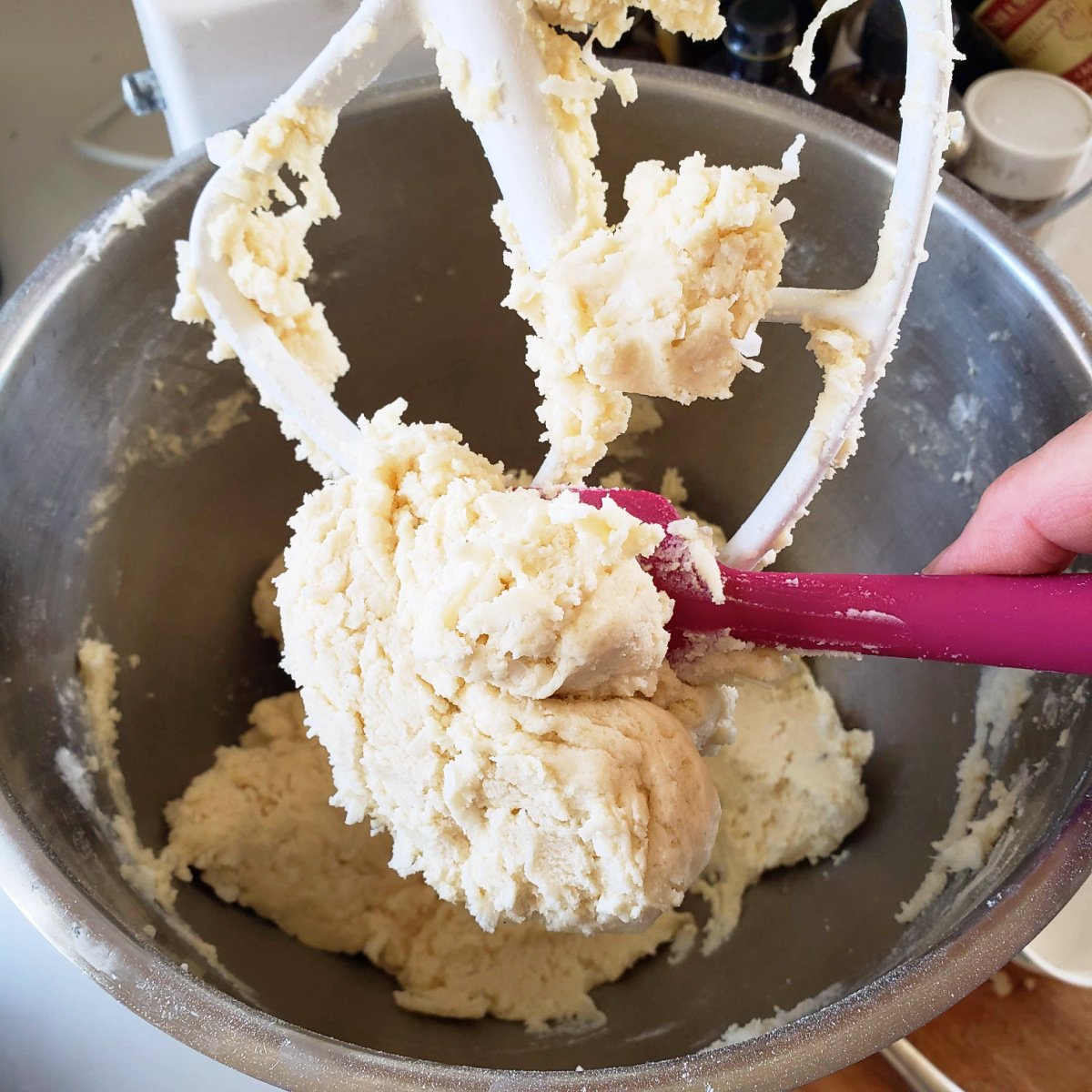 White cookie dough being scraped off a beater with a pink scraper for Coconut Lime Shortbread on ShockinglyDelicious.com