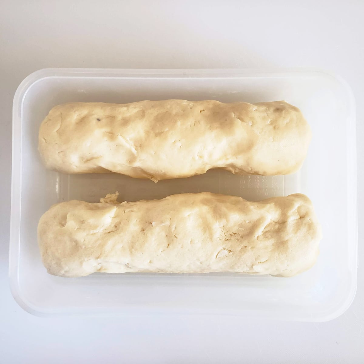 2 dough logs in a plastic container on a white cutting board