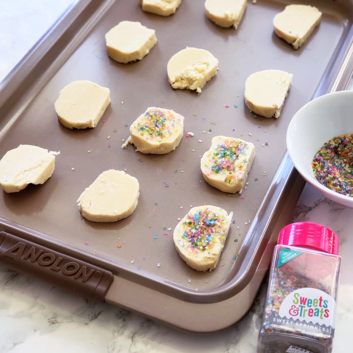 Raw cookie dough with colored sugar on top on baking sheet