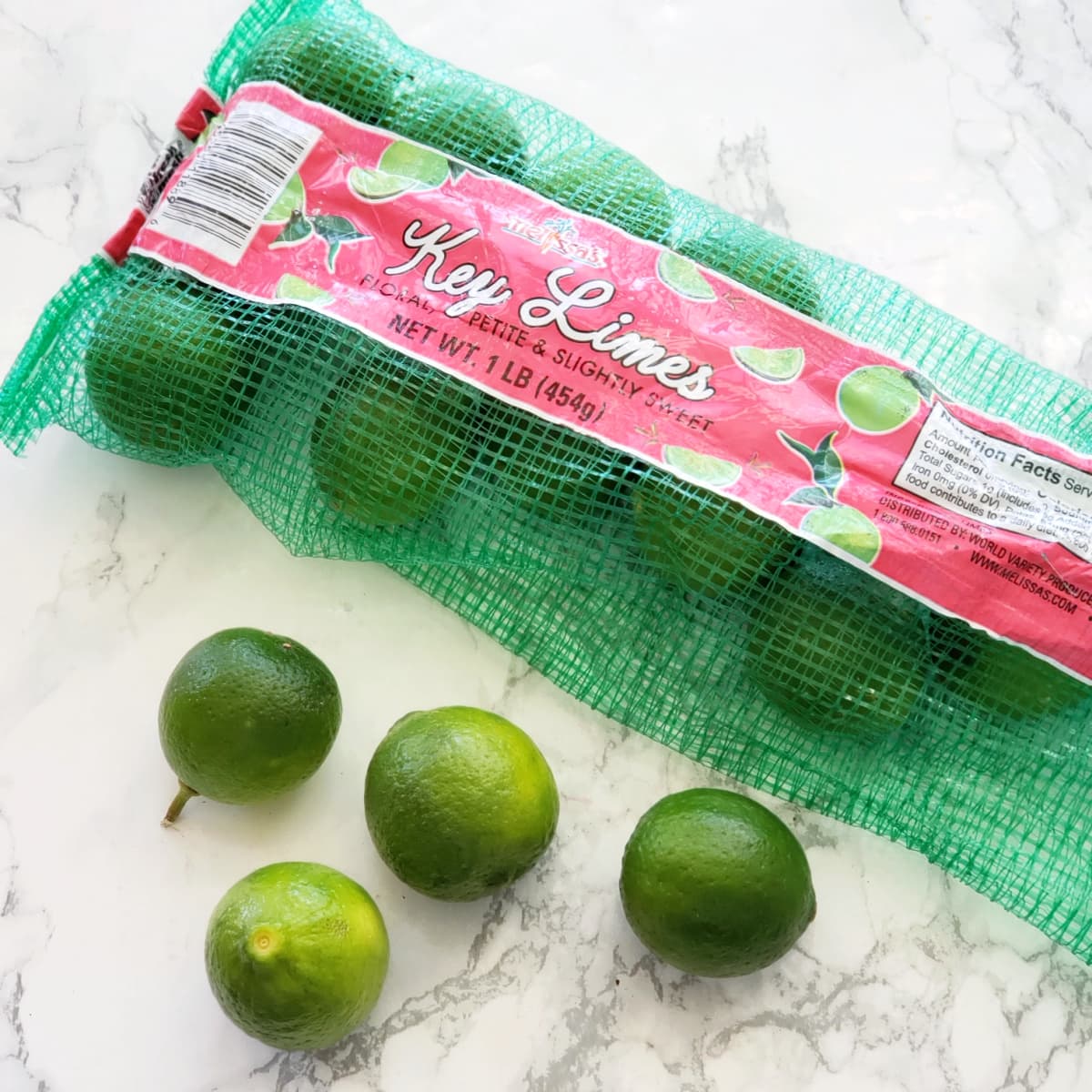 Key Limes in a bag on a white marble counter on ShockinglyDelicious.com