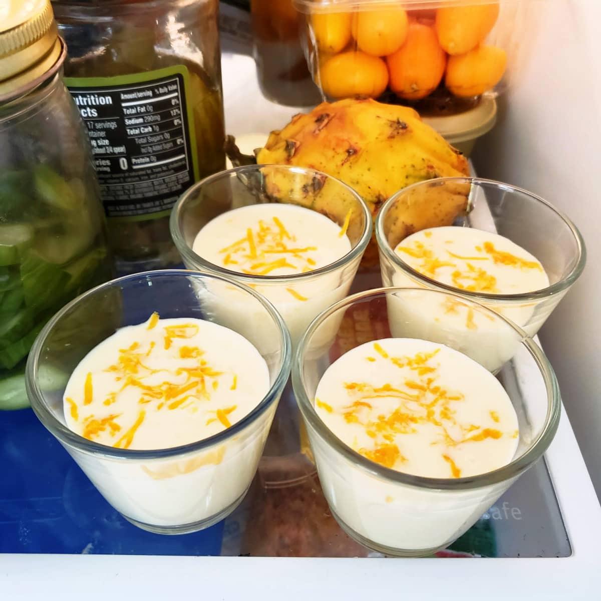 4 glasses with Meyer Lemon Posset are on a refrigerator shelf with other jars and items
