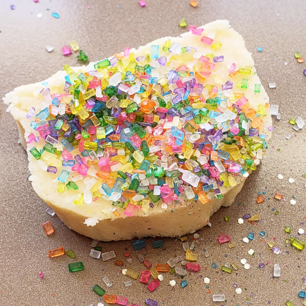 Bright colored sugar crystals piled onto a slice of cookie dough on a brown baking sheet