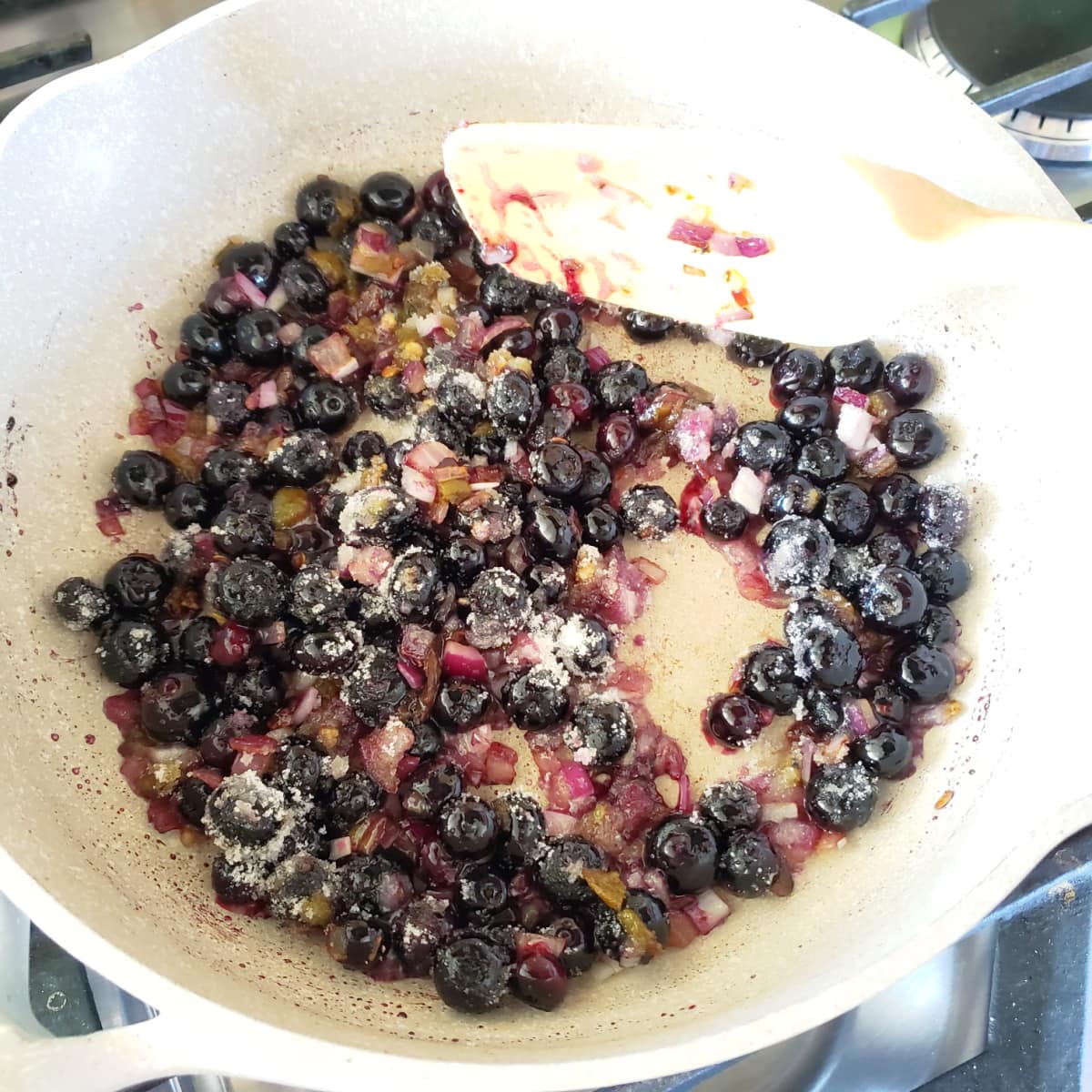 Blueberries, onion and Hatch chiles cook in a white skillet with a white spatulaous.com