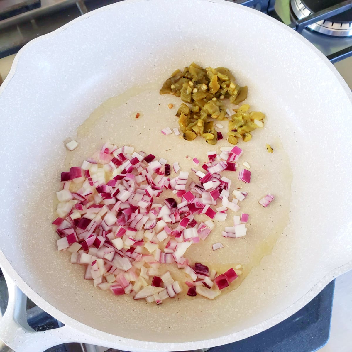 Chopped purple onion and green Hatch chile in a white skillet on a stovetop