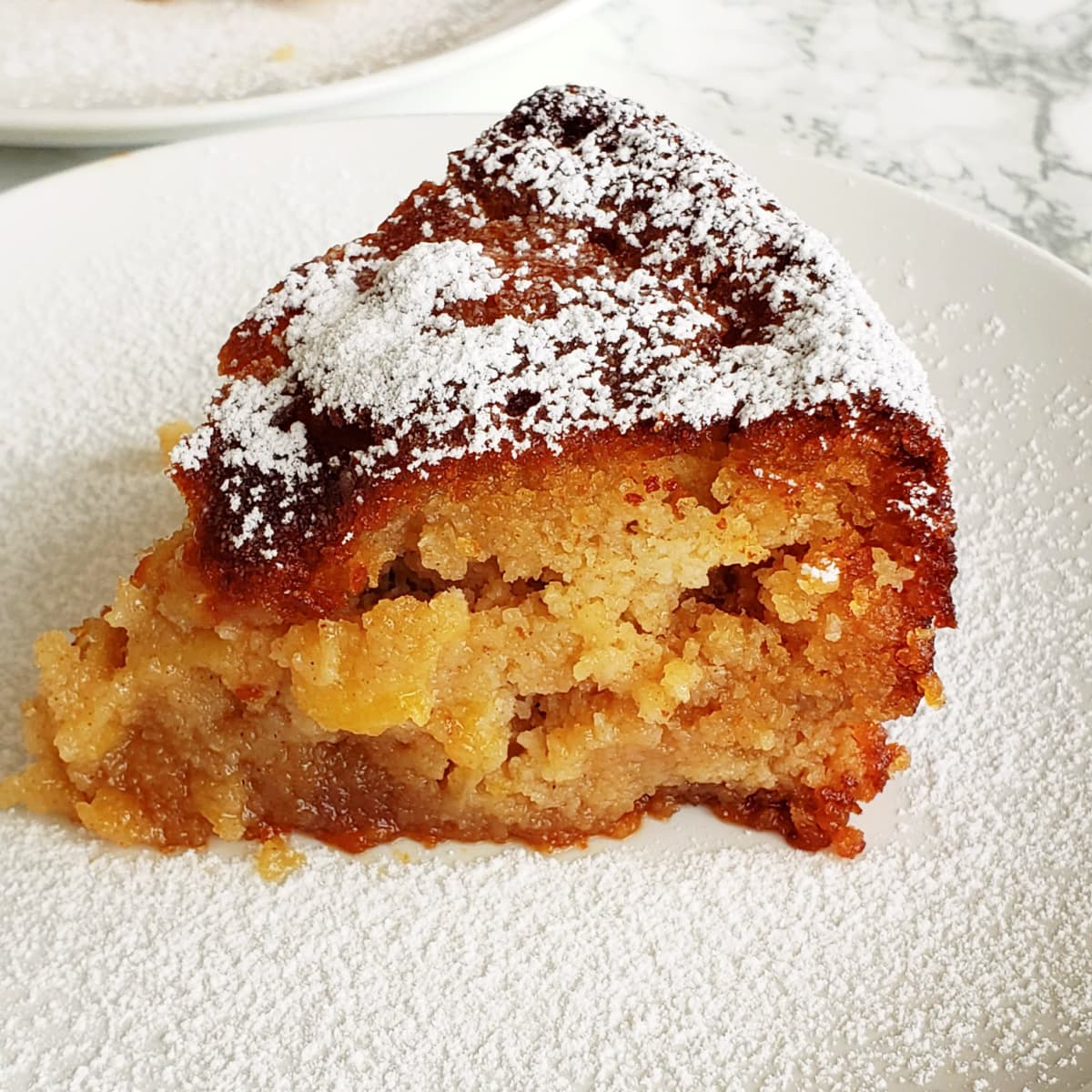 A wedge of Apple Almond Olive Oil Cake with powdered sugar sprinkled on top on a white plate
