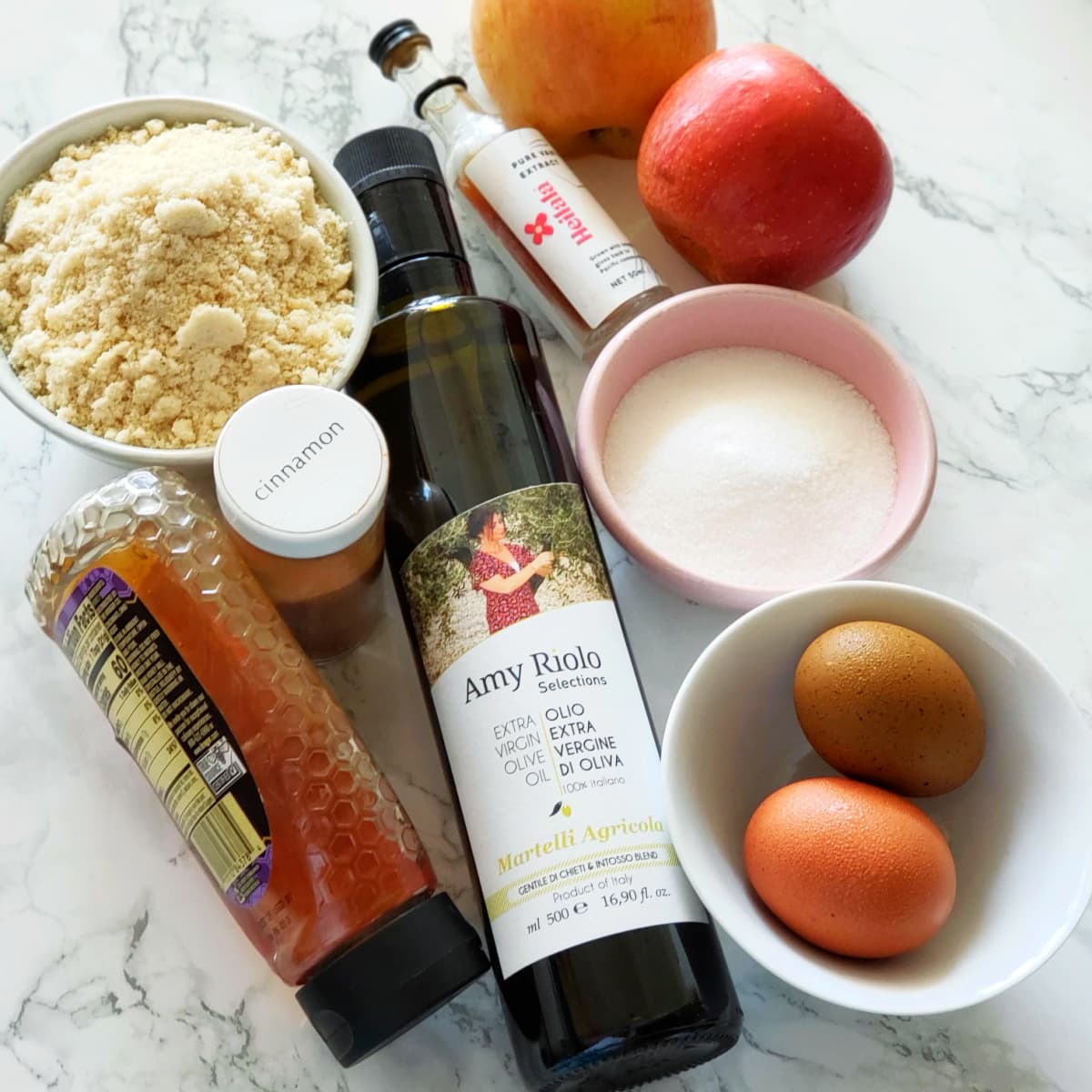 Ingredients for Apple Almond Olive Oil Cake laid out on a white marble counter top