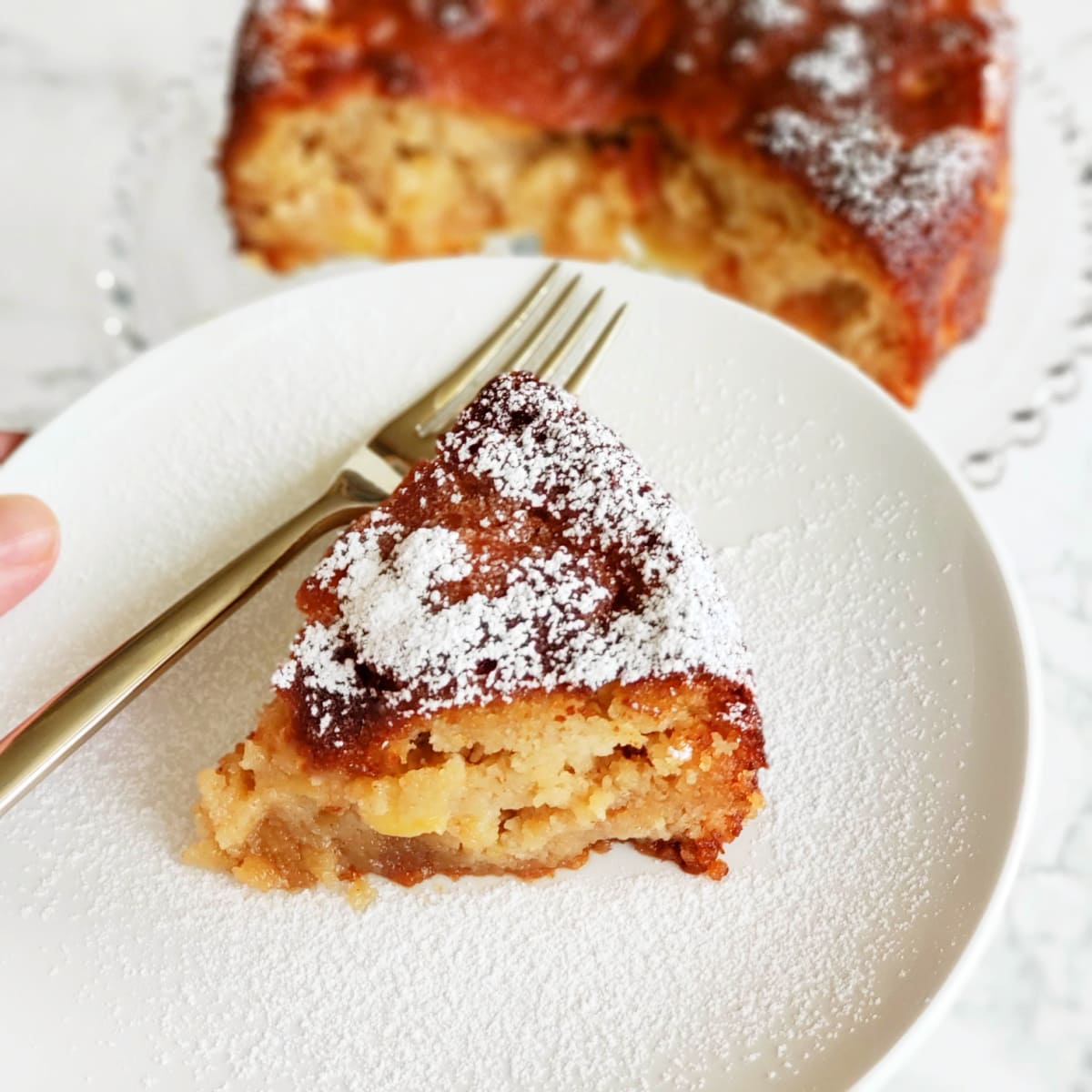 A wedge of Apple Almond Olive Oil small-batch cake on a white plate with a fork alongside