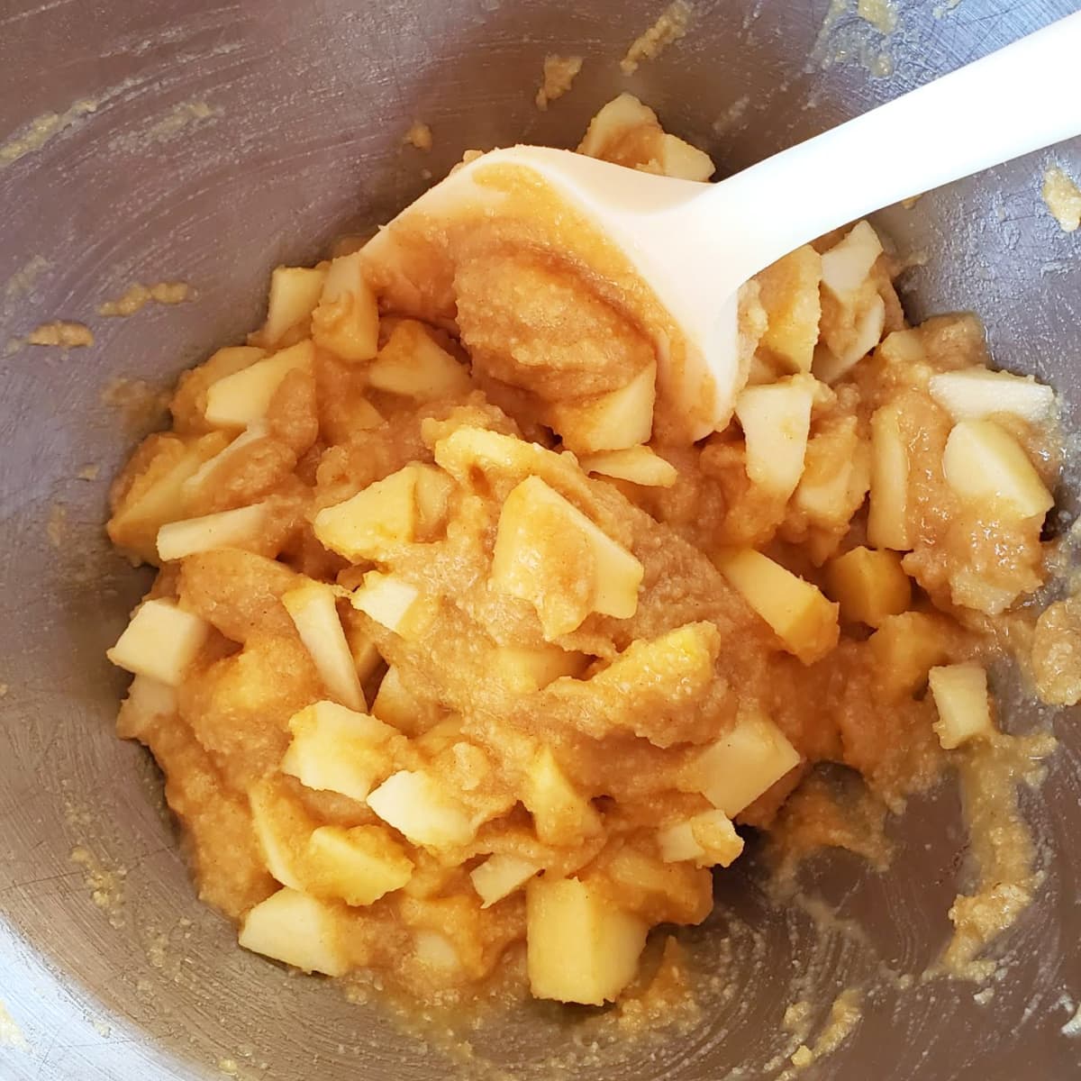 White spoon stirs chunky apples into batter in grey bowl
