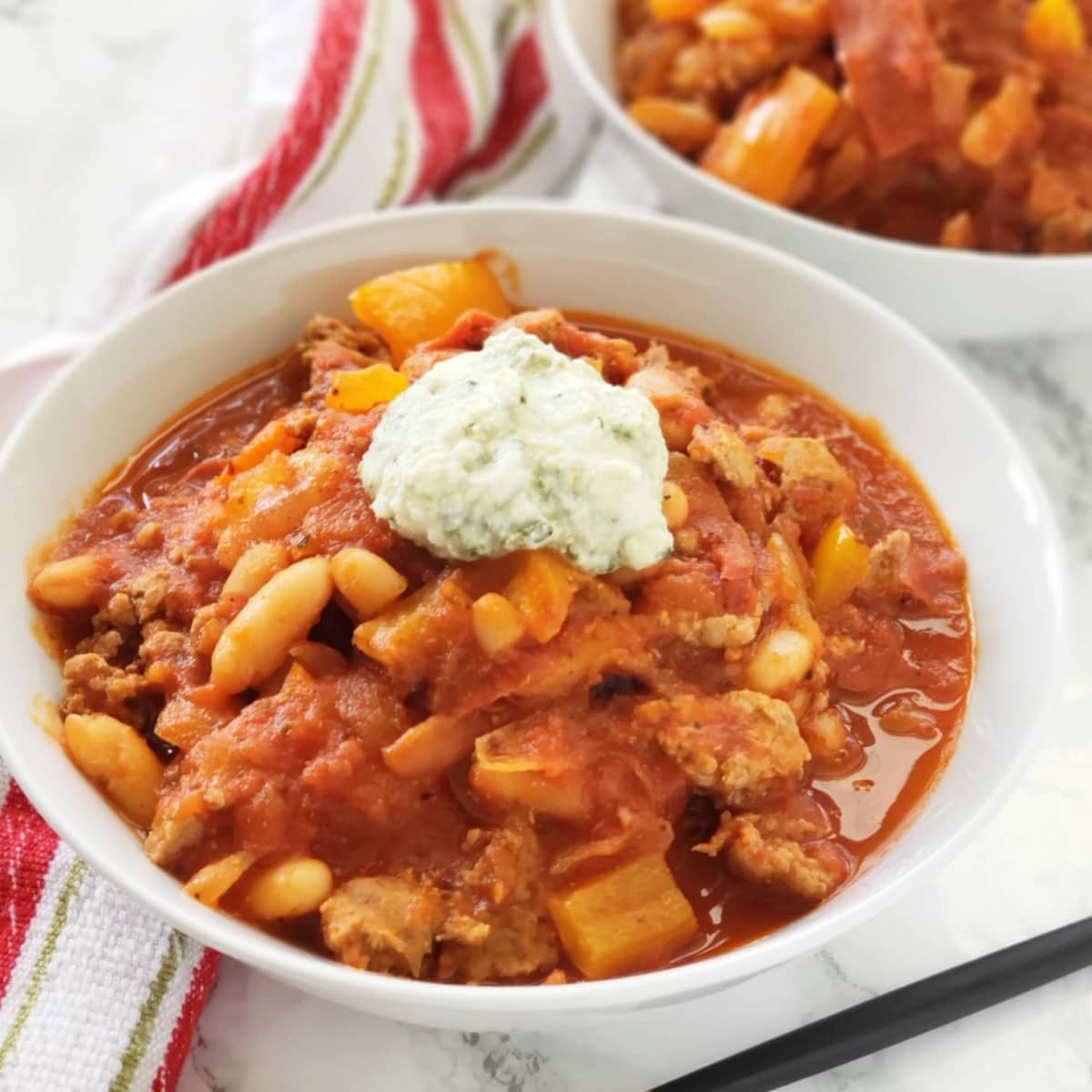 Pizza Chili in a white bowl with a dollop of ricotta on top and a spoon nestled alongside on ShockinglyDelicious.com