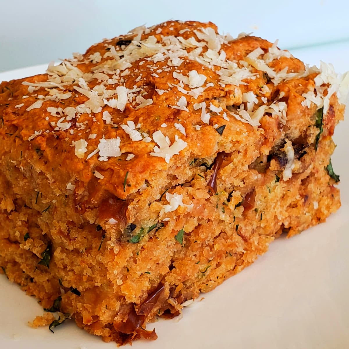 Closeup of a rectangularTomato Basil Biscuit on a white plate with shredded Parmesan on top