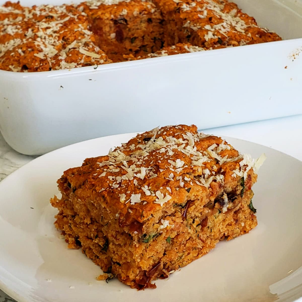 Tomato Basil Biscuit on a white plate with the baking dish behind