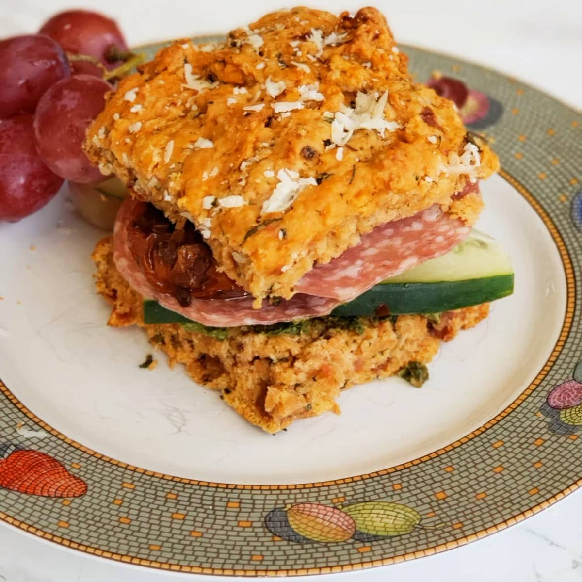 Stuffed sandwich on a white plate with grey rim and grapes behind it