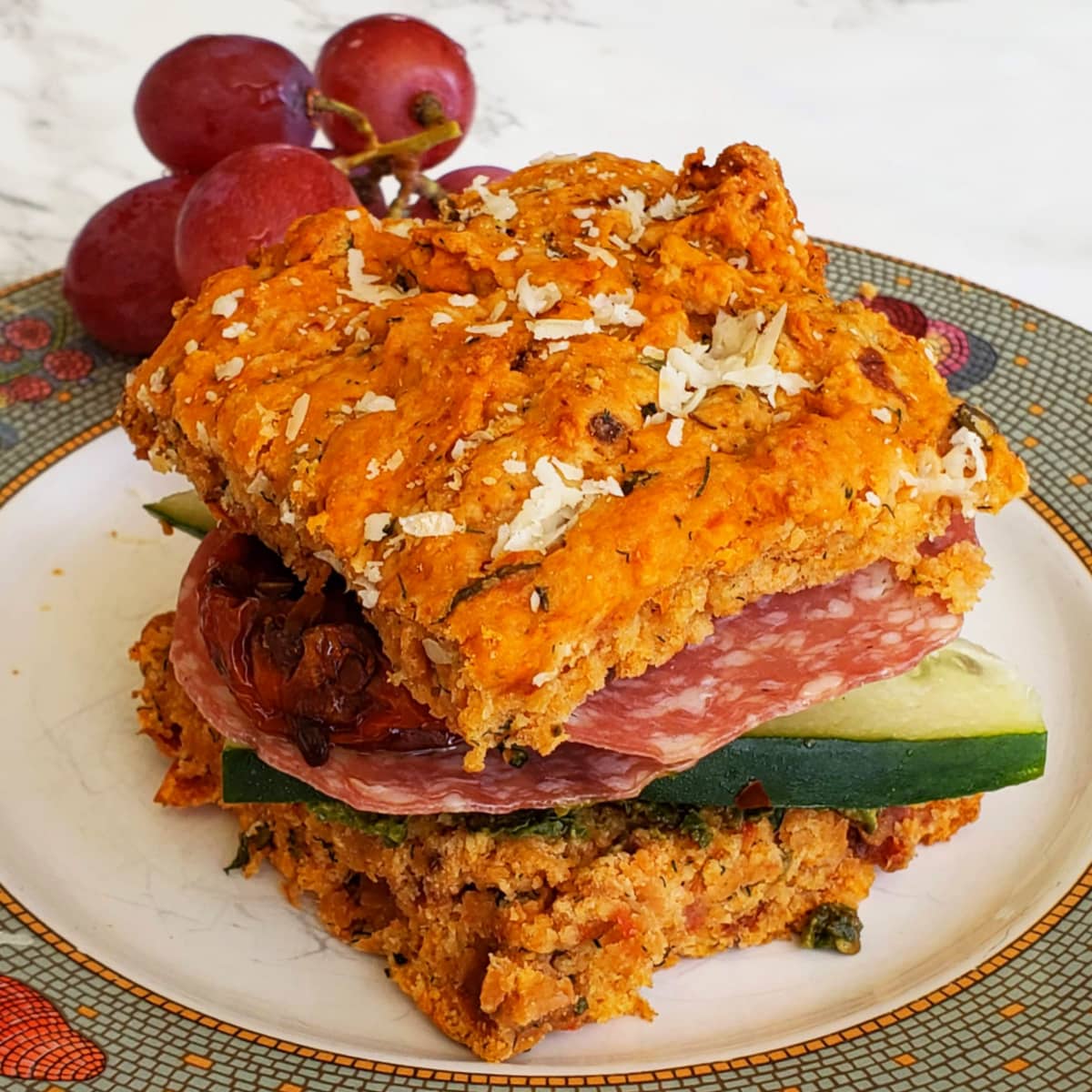 Tomato Basil Biscuit split and made into a sandwich on a white plate with a gray rim, with a bunch of grapes behind it