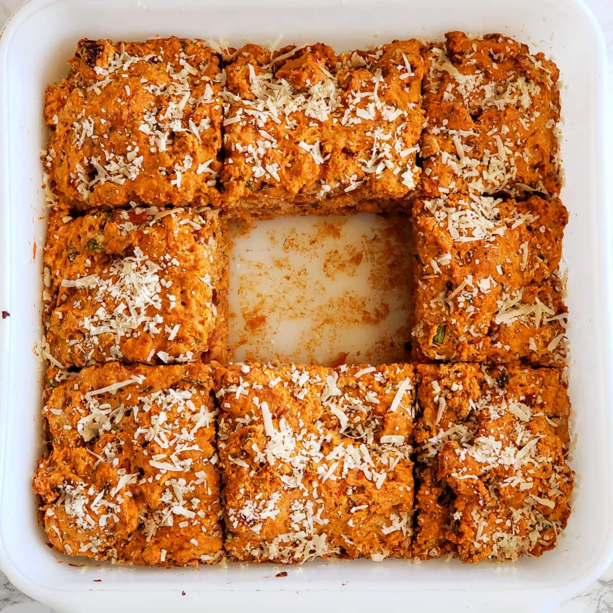 1 piece missing from the center of Tomato Basil Biscuits baked in a white baking dish