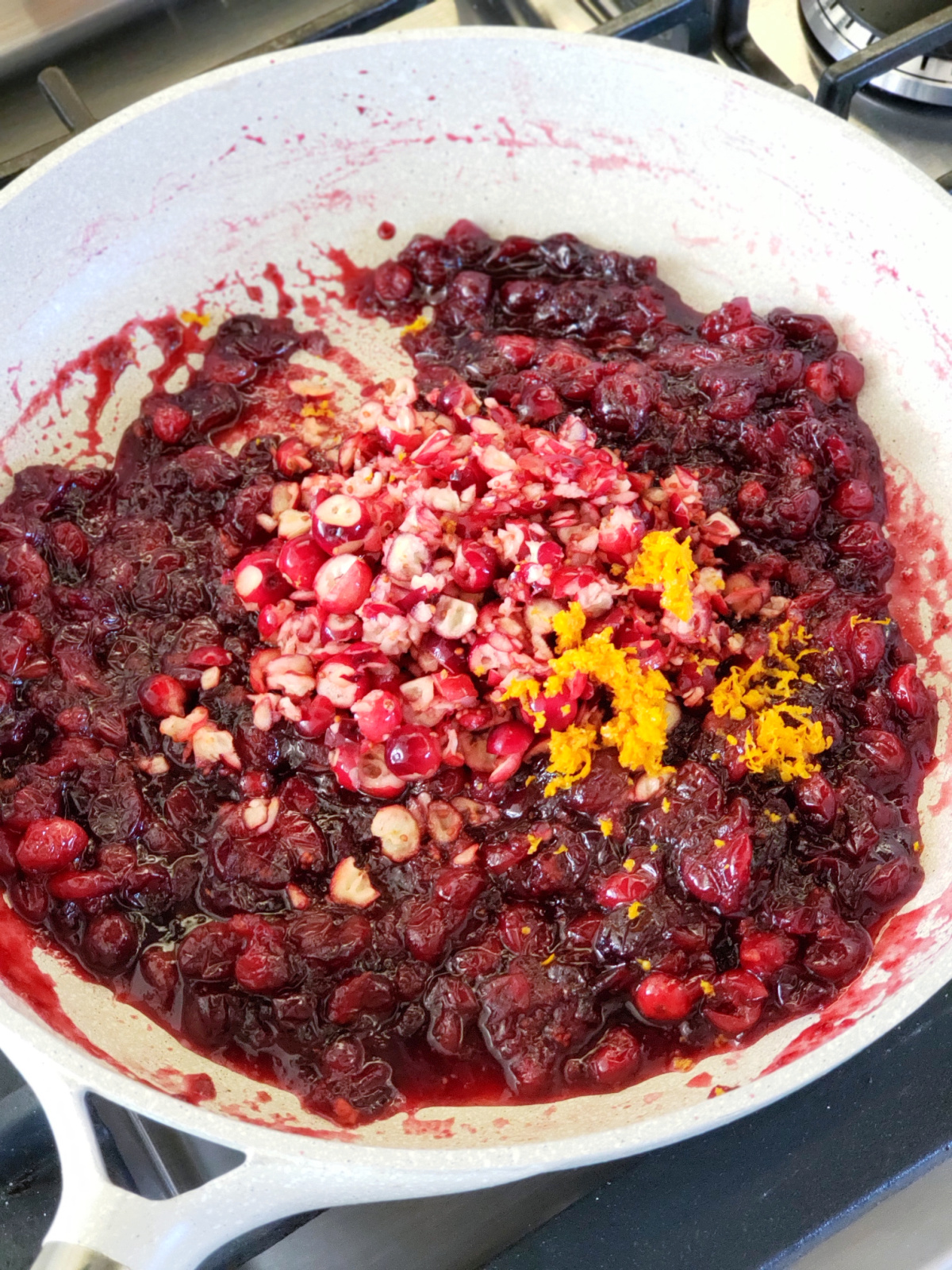 Fresh chopped cranberries and orange zest are added to the cooked cranberries in the white skillet