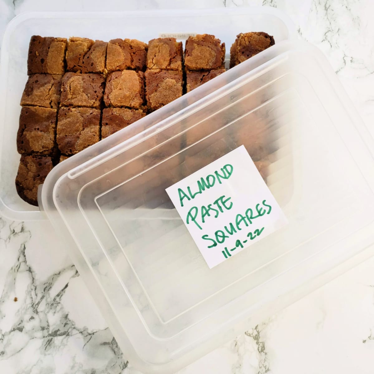 Almond Paste Squares packed for freezing in a plastic container with a label on the lid