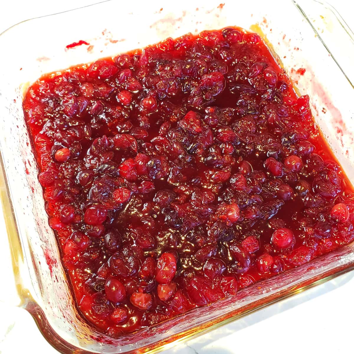 Baked Cranberry Sauce with Orange Liqueur in a clear glass square baking dish out of the oven on ShockinglyDelicious.com