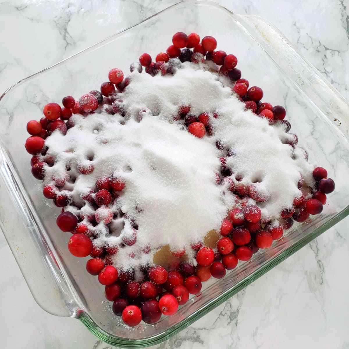 Clear glass baking dish with cranberries and lots of sugar
