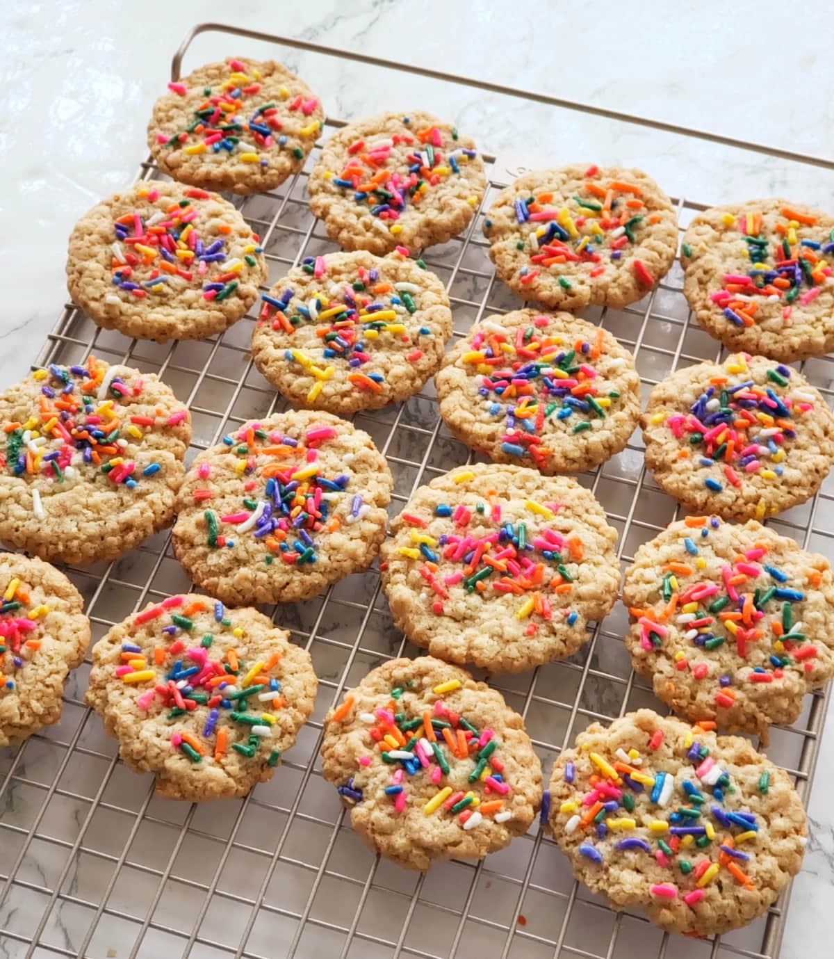 16 Oatmeal Shortbread Cookies with colorful sprinkles on top cooling on a cooling rack on a white marble countertop