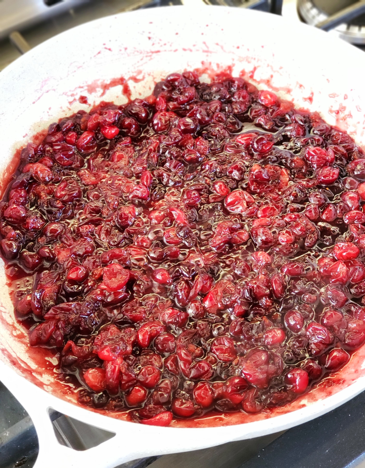 Thickened cranberries get jammy in a white skillet as they cook