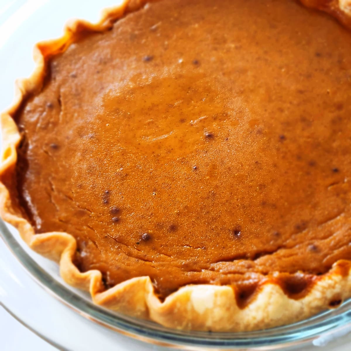 Partial view of a whole Eggnog Pumpkin Pie in a clear glass pie dish on ShockinglyDelicious.com