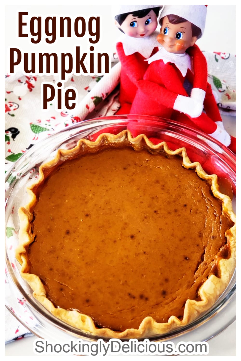 A whole Eggnog Pumpkin Pie in a glass pie dish with 2 Elves on the Shelf behind the pie, and recipe title superimposed 