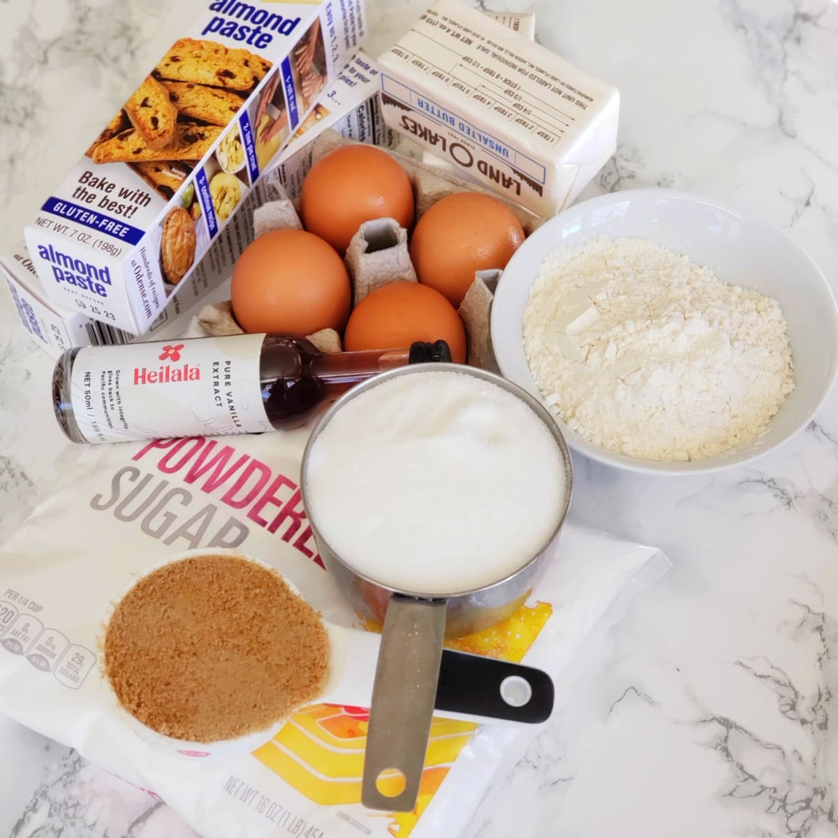 Various ingredients for Almond Paste Squares laid out on a white marble countertop