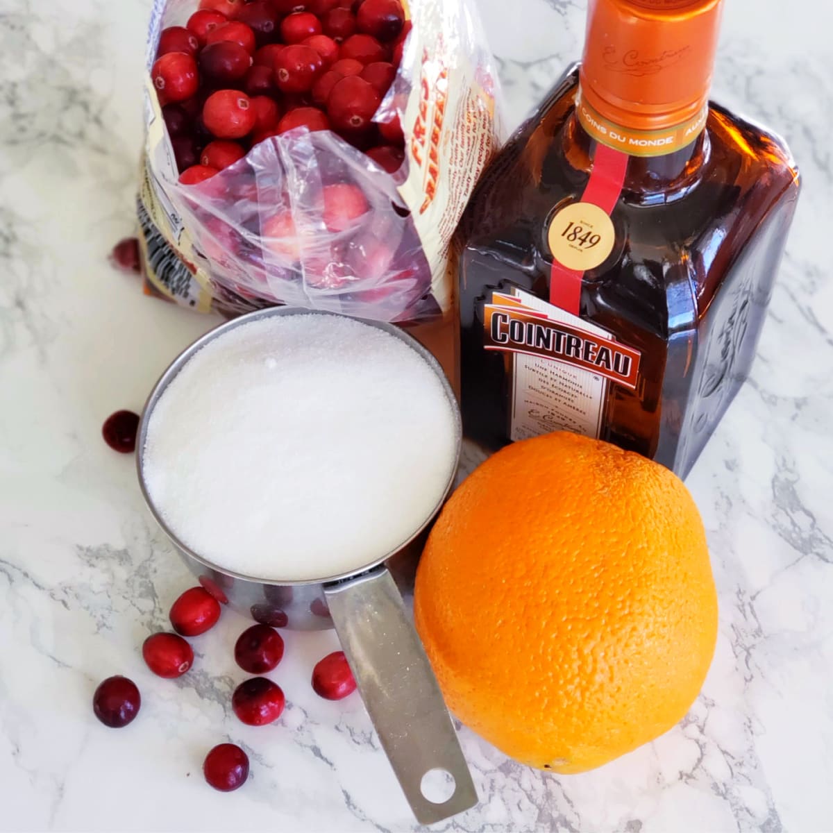 Ingredients for Baked Cranberry Sauce with Orange Liqueur laid out on a white marble countertop