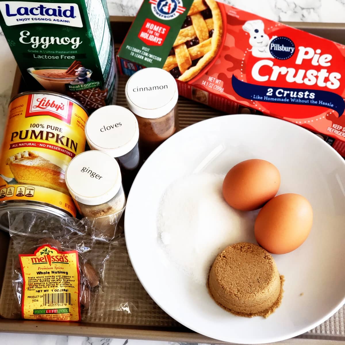 Ingredients for Eggnog Pumpkin Pie placed on a gold baking sheet