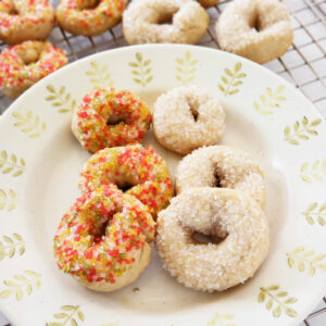 Donut-shaped cookies on a plate with additional cookies in the background on a cooling rack