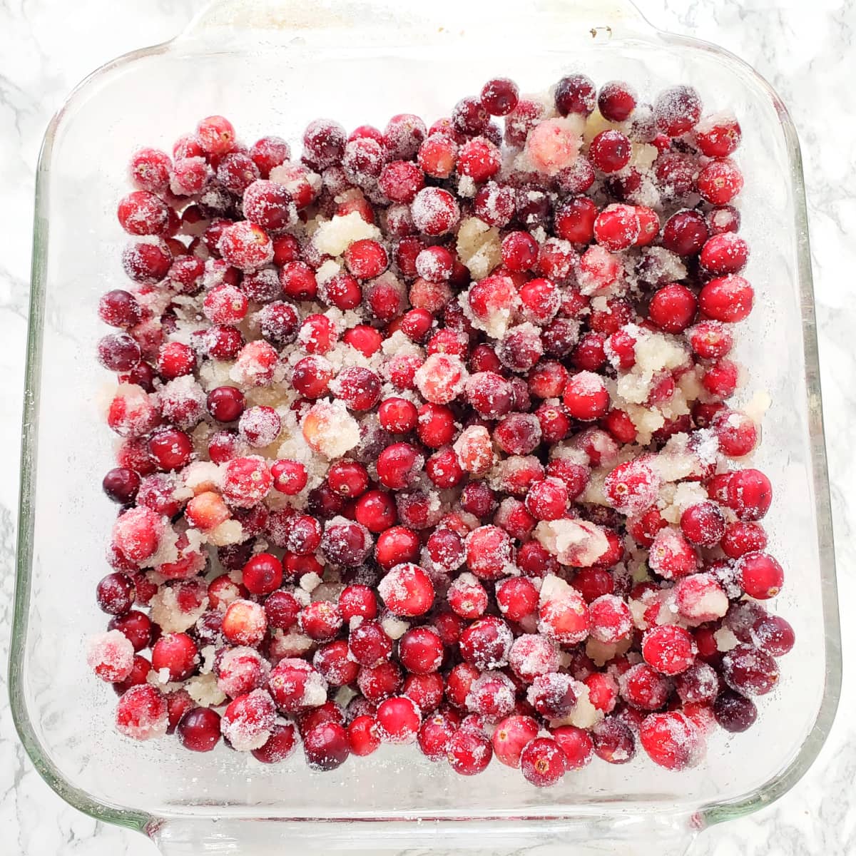 Cranberries, sugar and orange juice mixed in clear glass baking dish