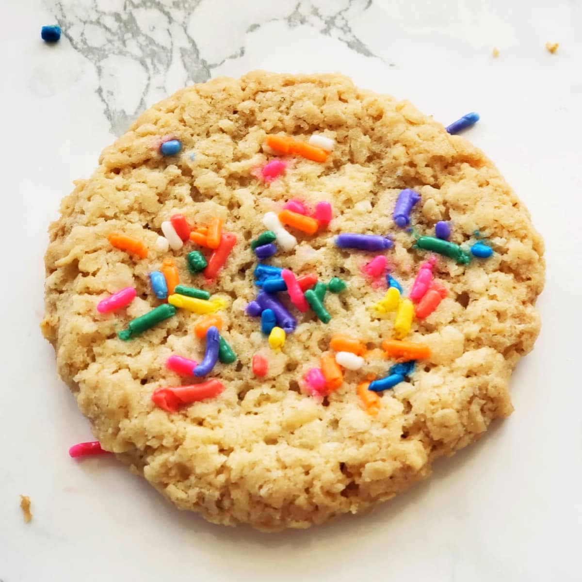 Single cookie with colorful sprinkles on top on a white marble counterop