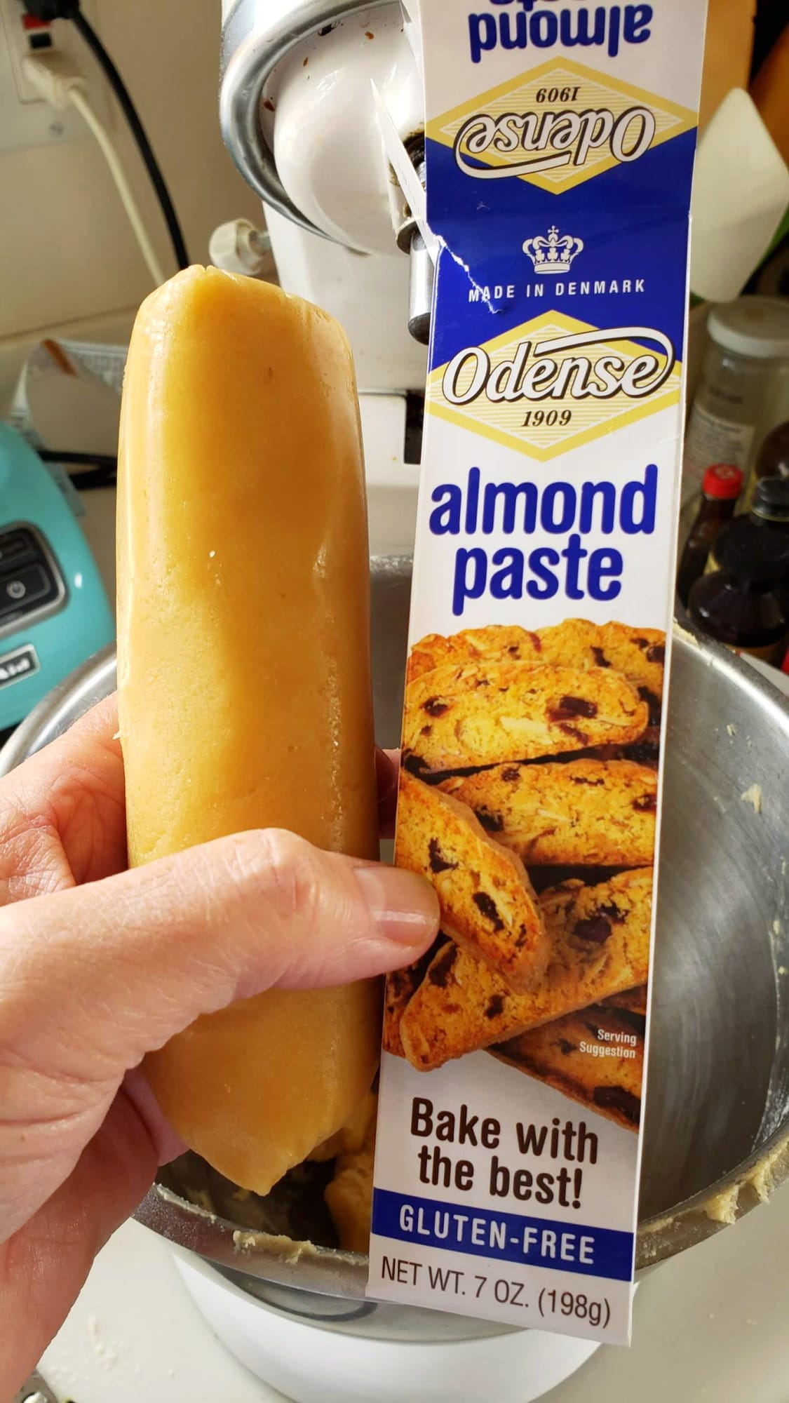 Hand holding a cylinder of Odense almond paste out of the wrapper next to the box