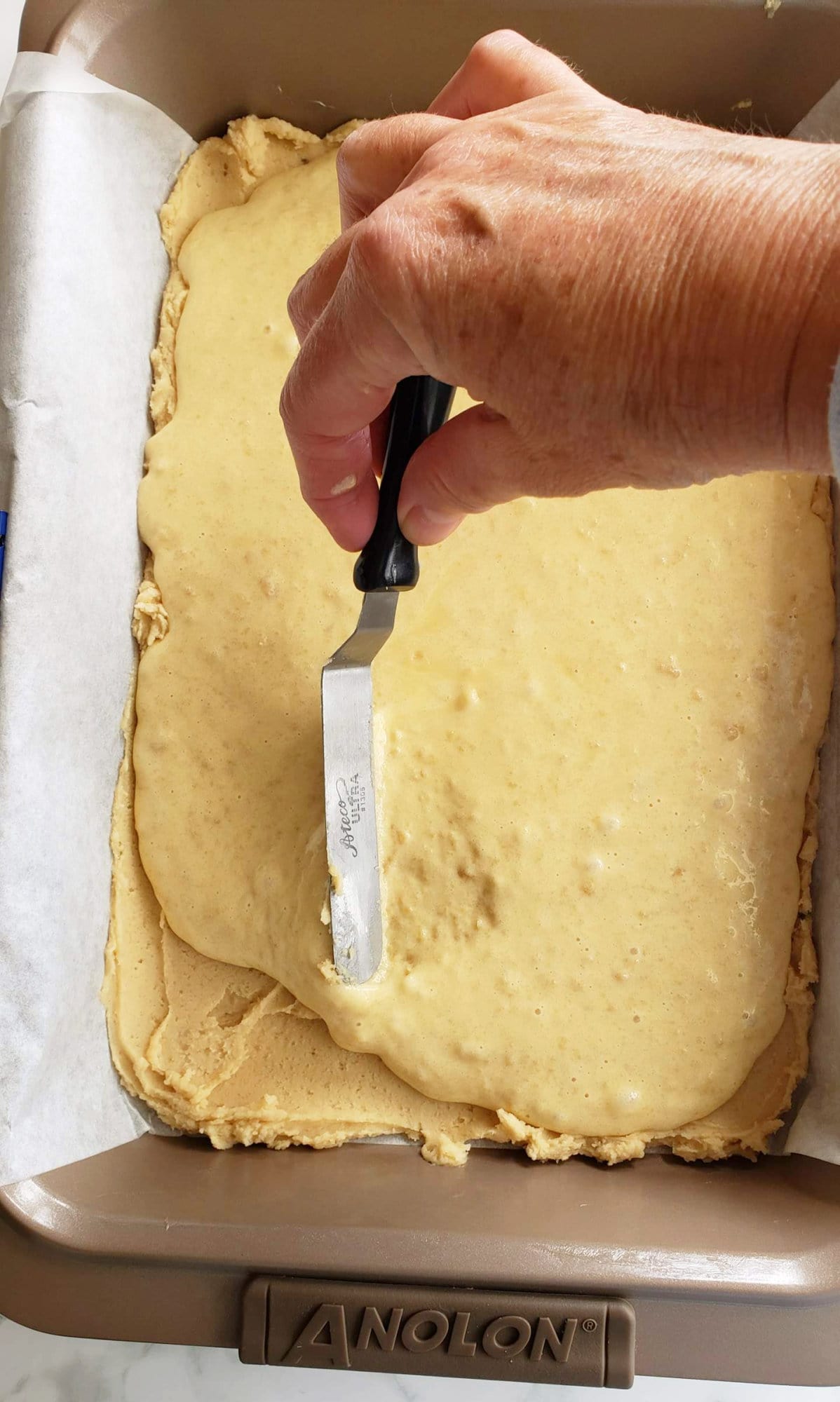 Hand holding offset spatula spreads filling over prepared crust