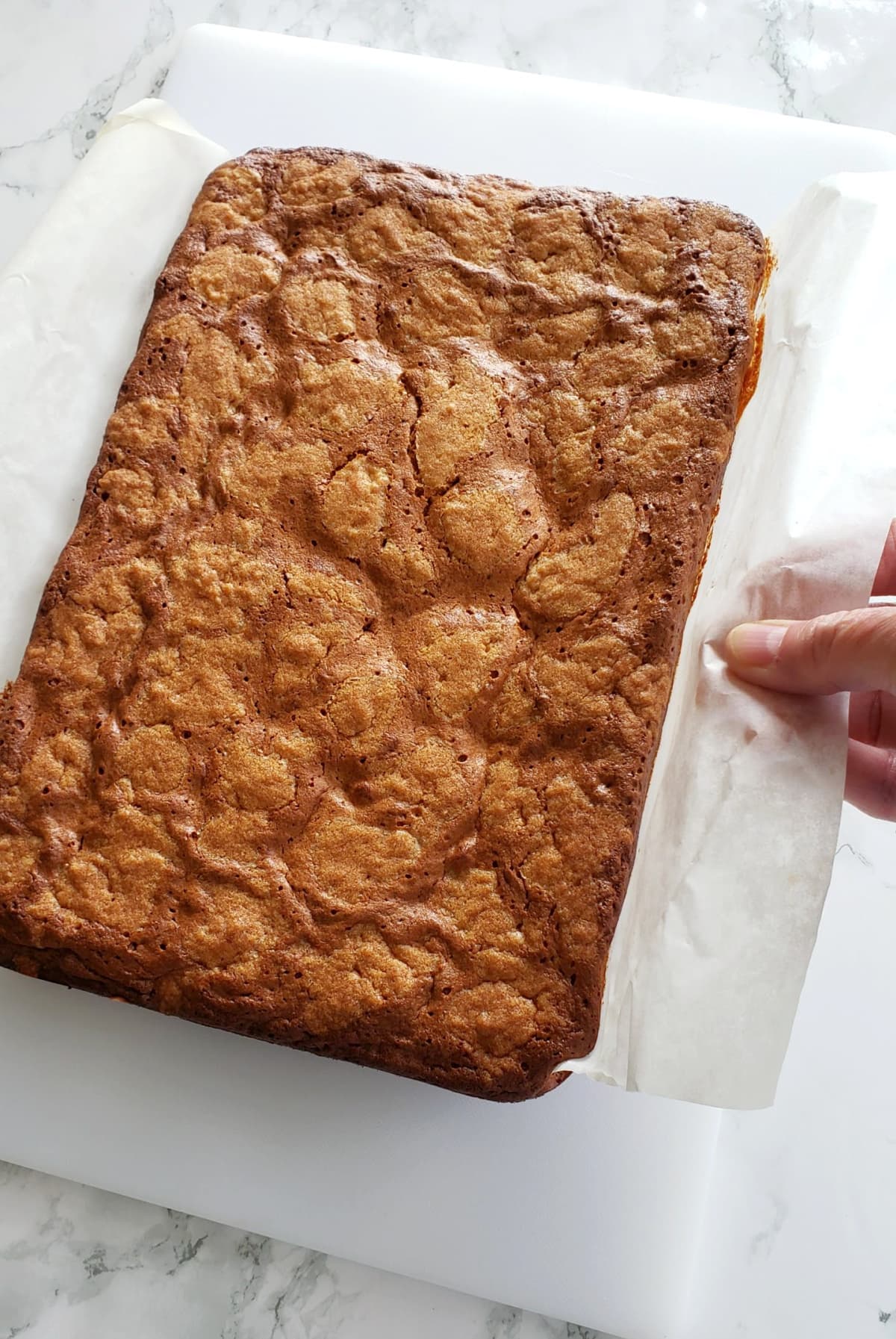 Hand tugs on parchment paper sling to place bars in a single piece on a white cutting board