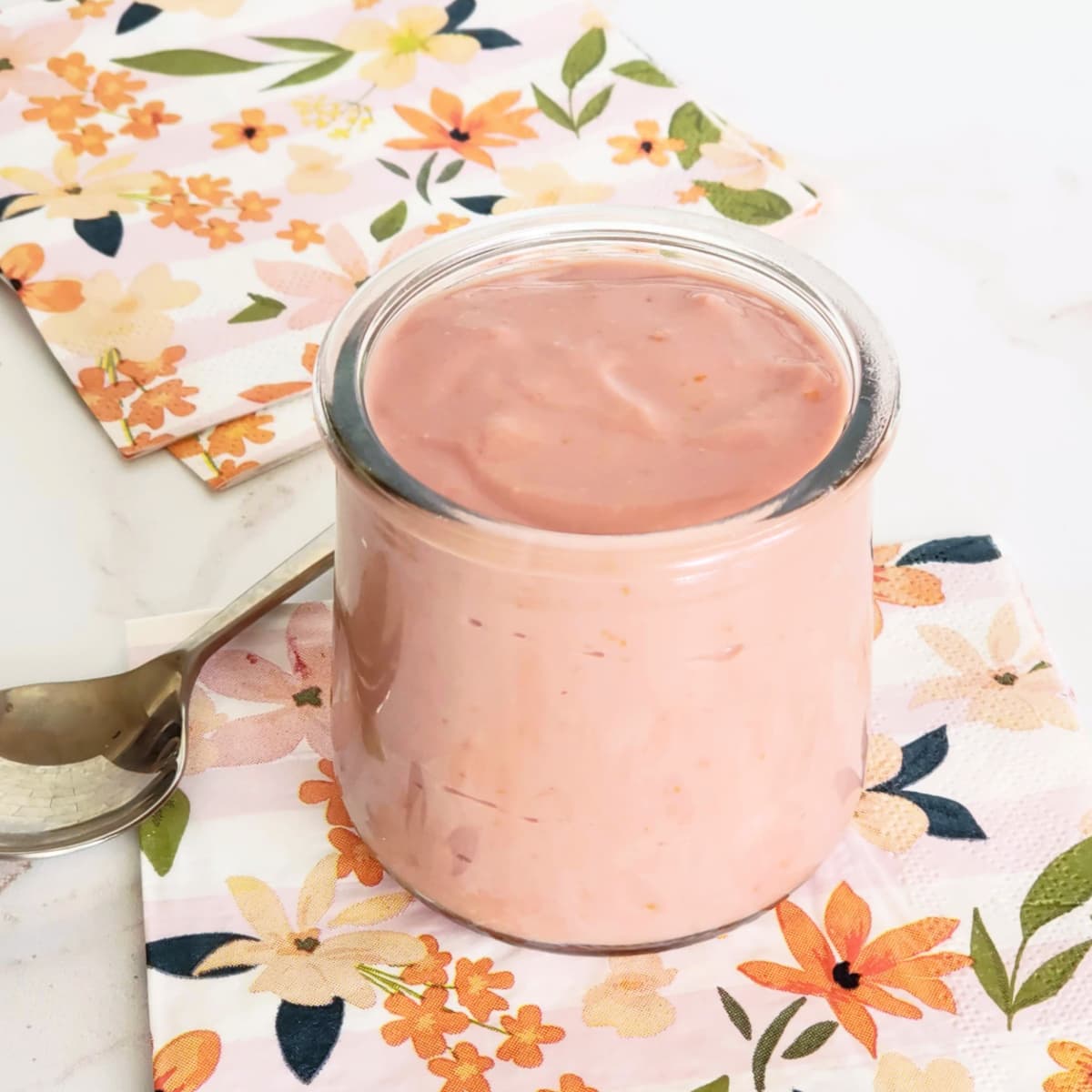 Clear glass jar of orange curd sits atop several flowered napkins with a spoon to the left