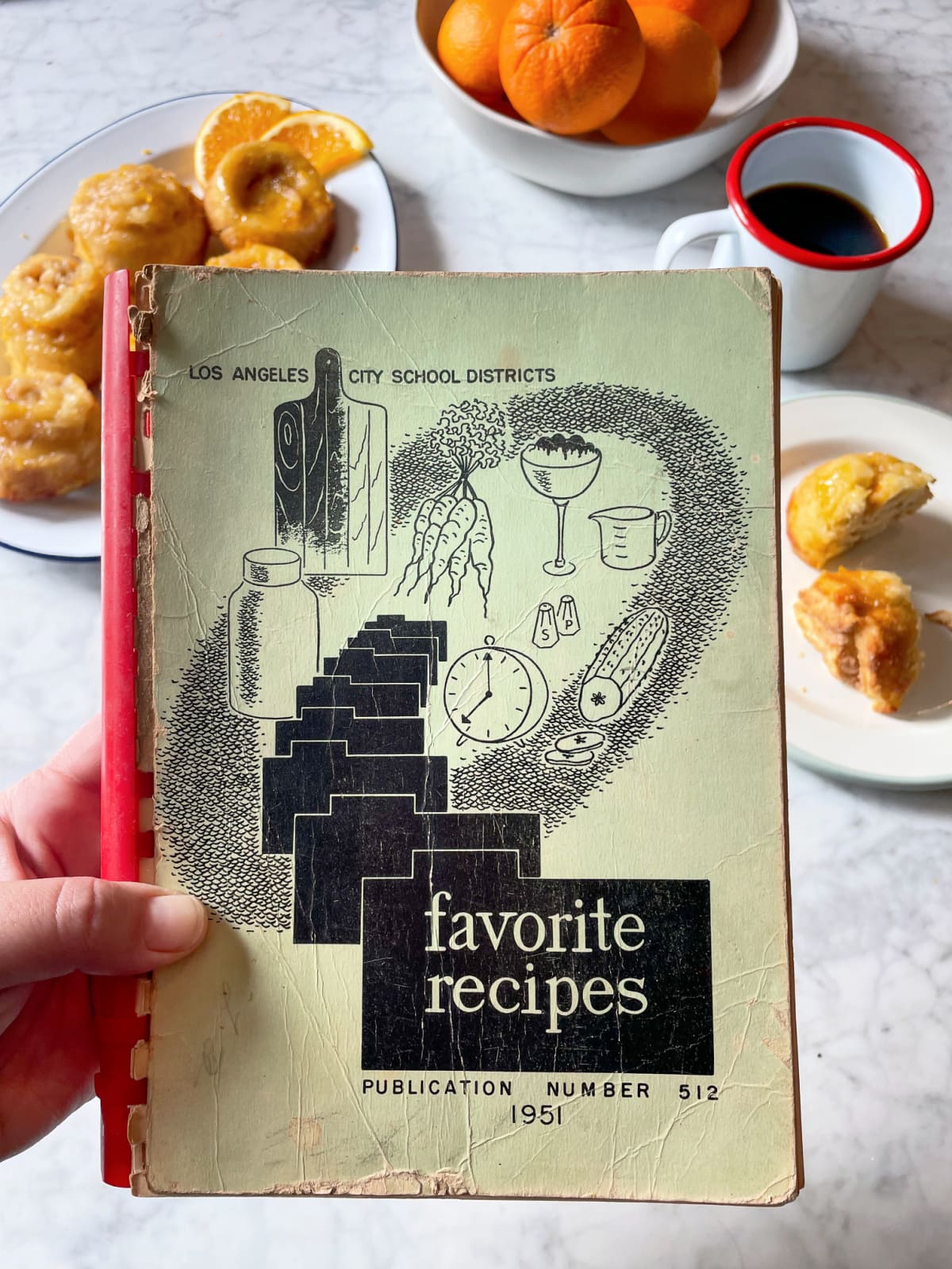 Weathered cookbook held by a hand with biscuits on plates in the background