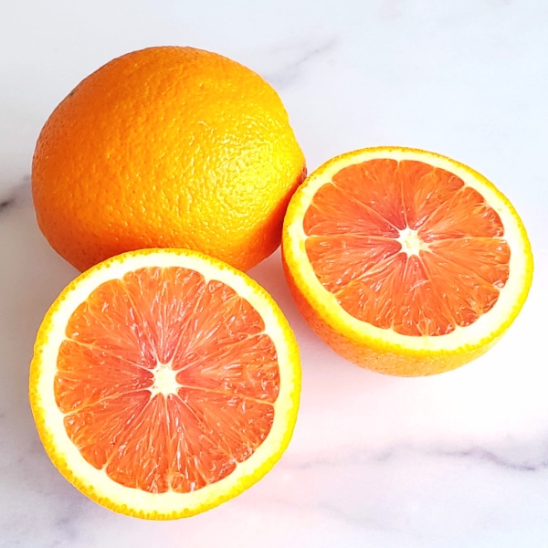 1 whole orange and 2 orange halves showing inside segments on a white marble counter