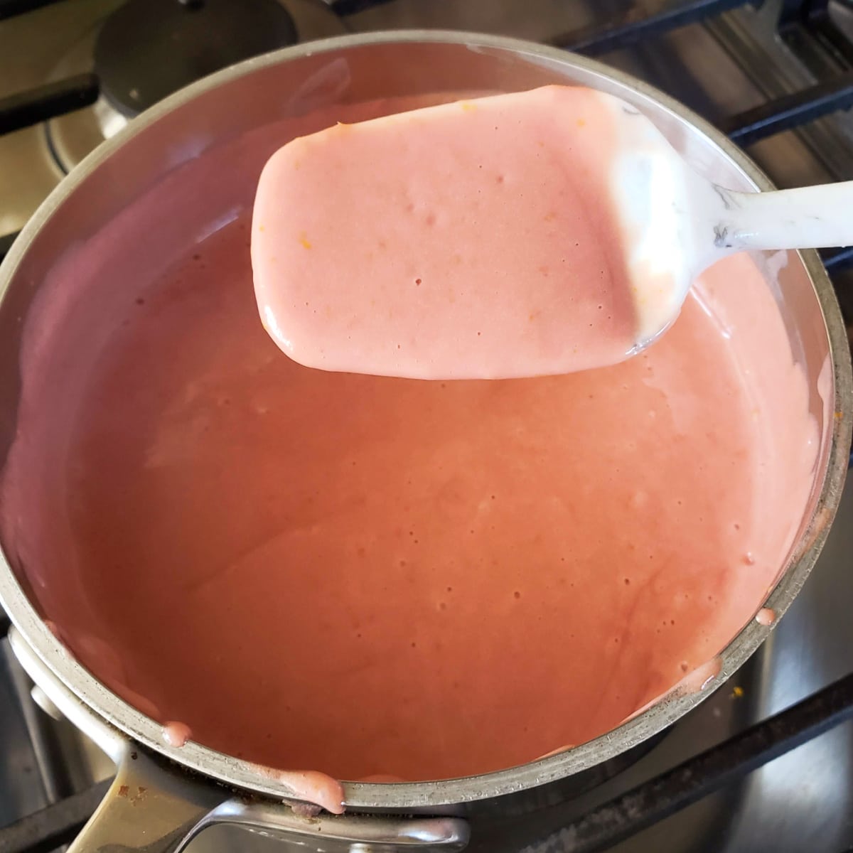 White spatula with orange curd on it sits above a saucepan with the rest of the curd