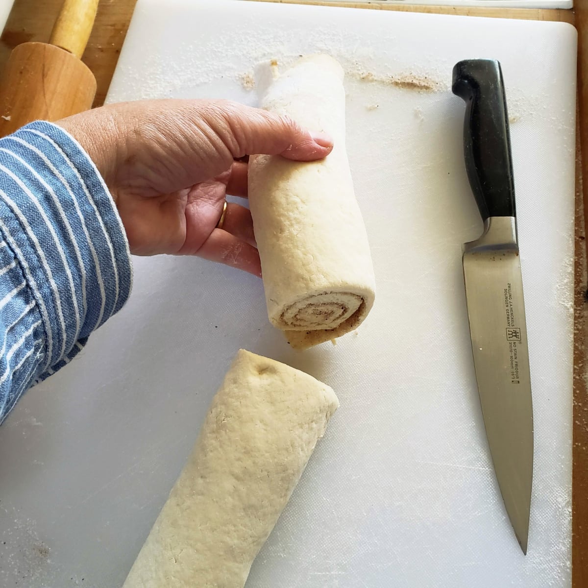 A hand holds half the dough log with a knife alongside on a white cutting board