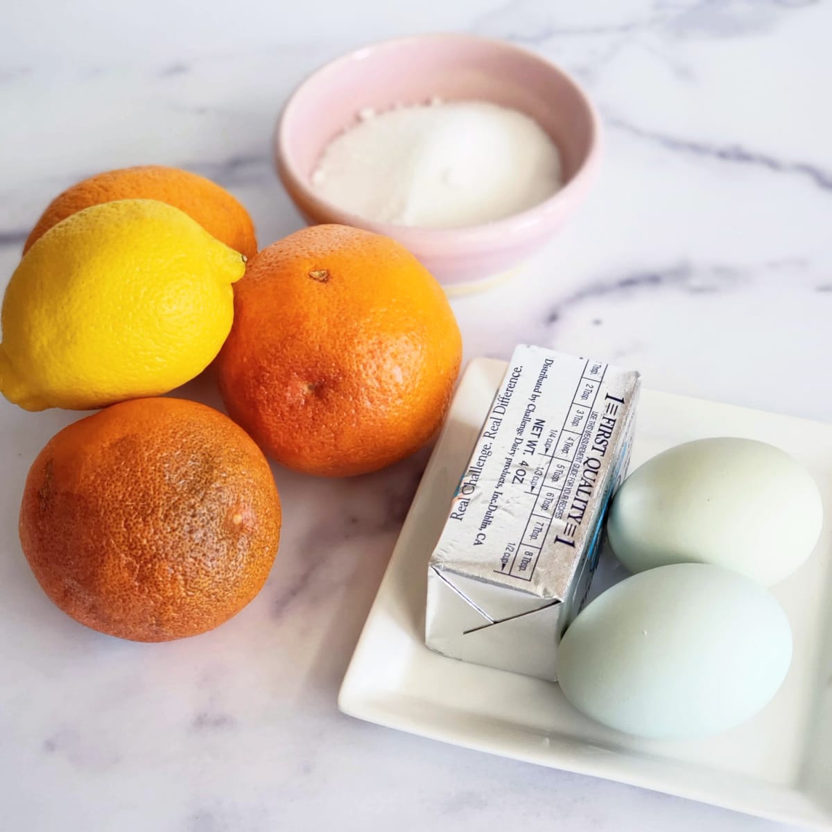 An array of ingredients for orange curd on a white marble countertop 