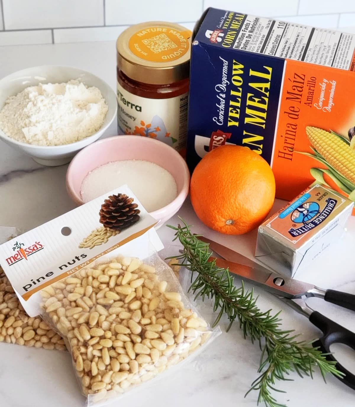 Ingredients for Rosemary Pine Nut Cornmeal Shortbread gathered on a white marble counter