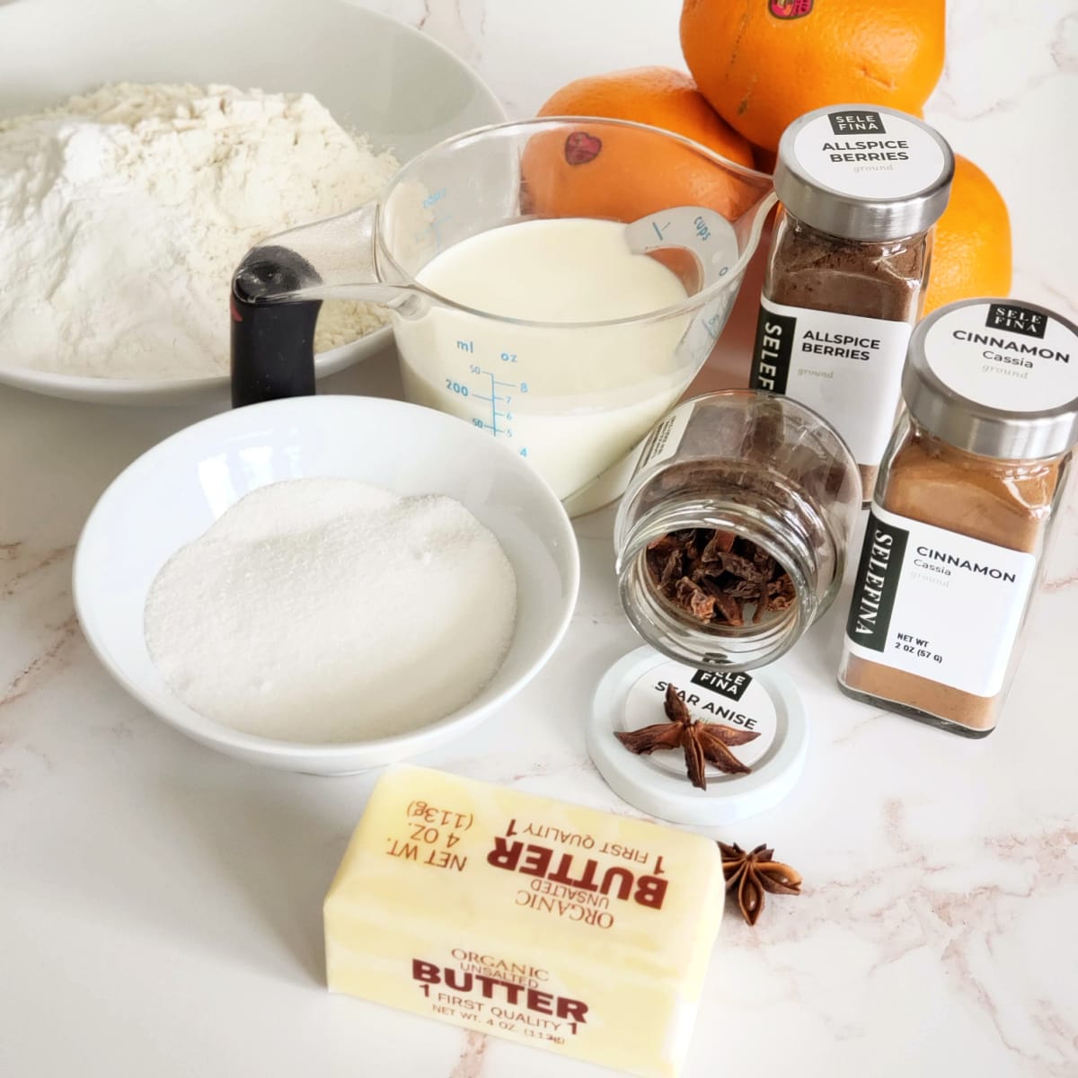 Ingredients for Sticky Spiced Orange Biscuits grouped on pink marble countertop 