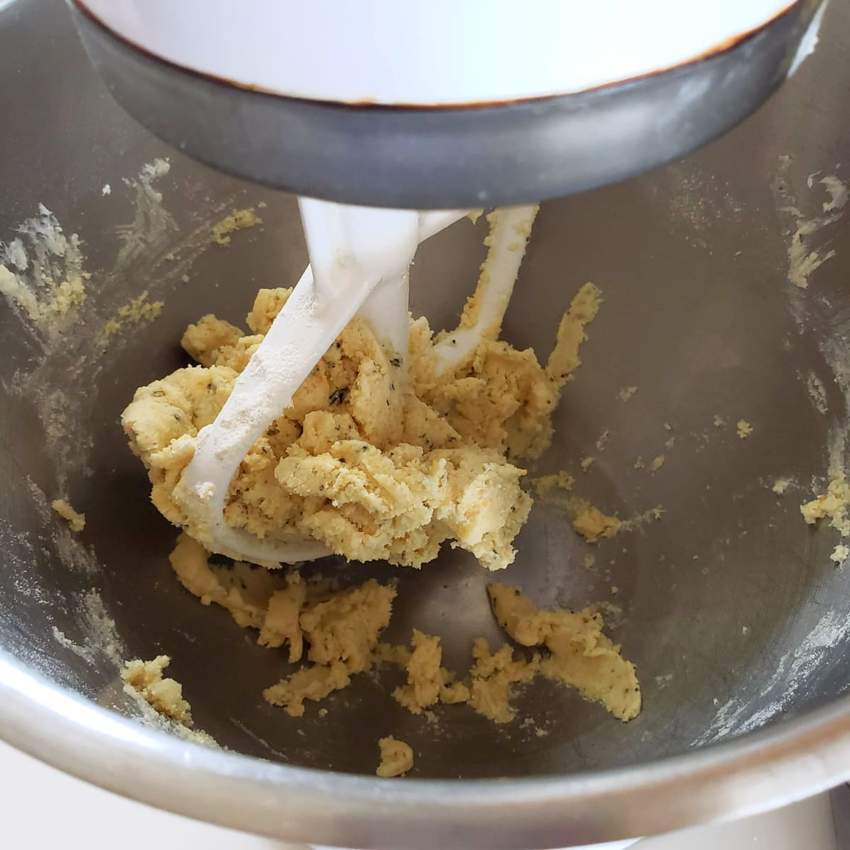 Cookie dough clumps around the white paddle in silver mixing bowl