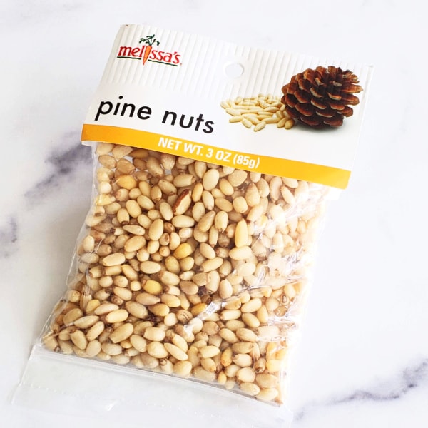 Clear bag of light brown pine nuts on a white marble counter