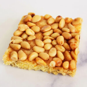 Square bar cookie Rosemary Pine Nut Cornmeal Shortbread rests on a white marble countertop