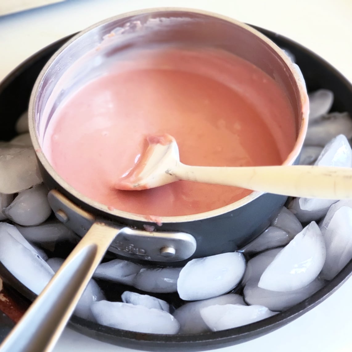 Saucepan with orange curd in it sits in a gray skillet filled with ice