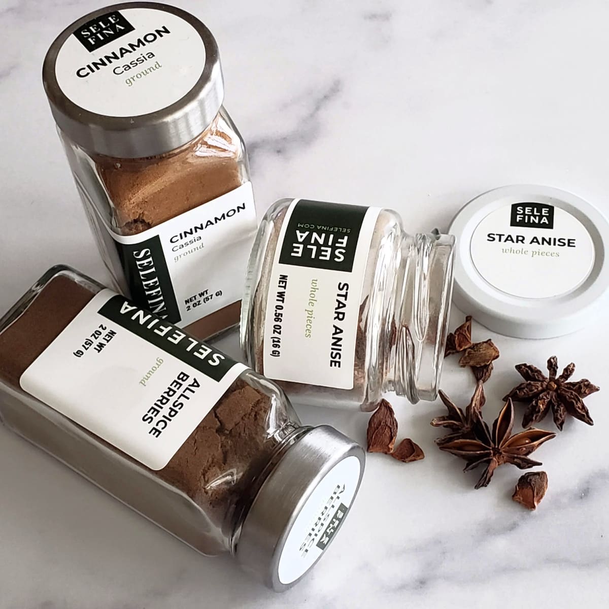 Jars of cinnamon, allspice and star anise on a white marble countertop