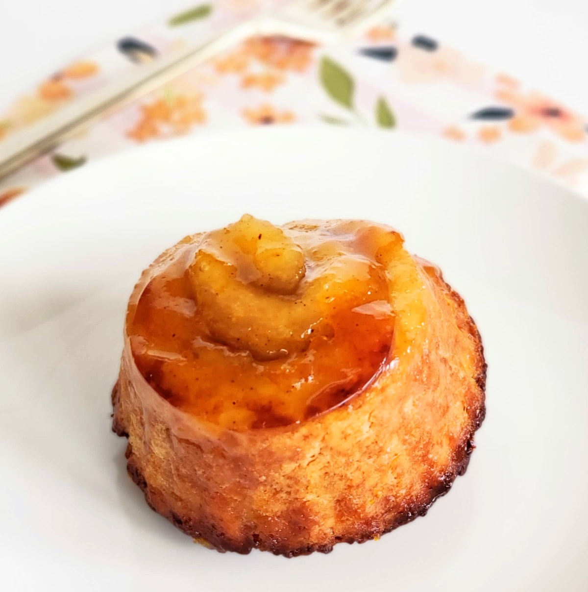 Orange spiral biscuit on a white plate with flowered napkin and fork behind.